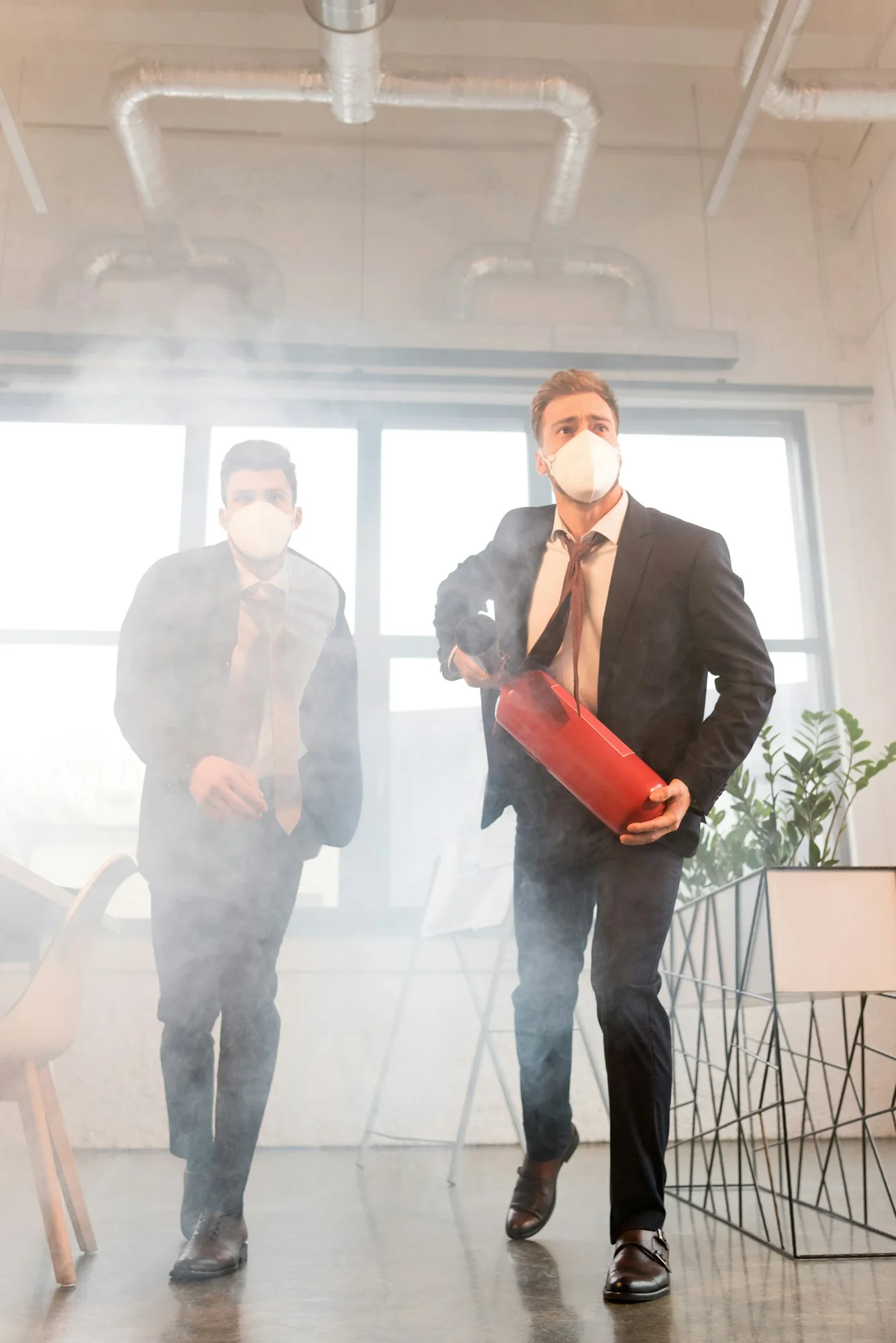 businessman in mask holding extinguisher near colleague while walking in office with smoke jpg